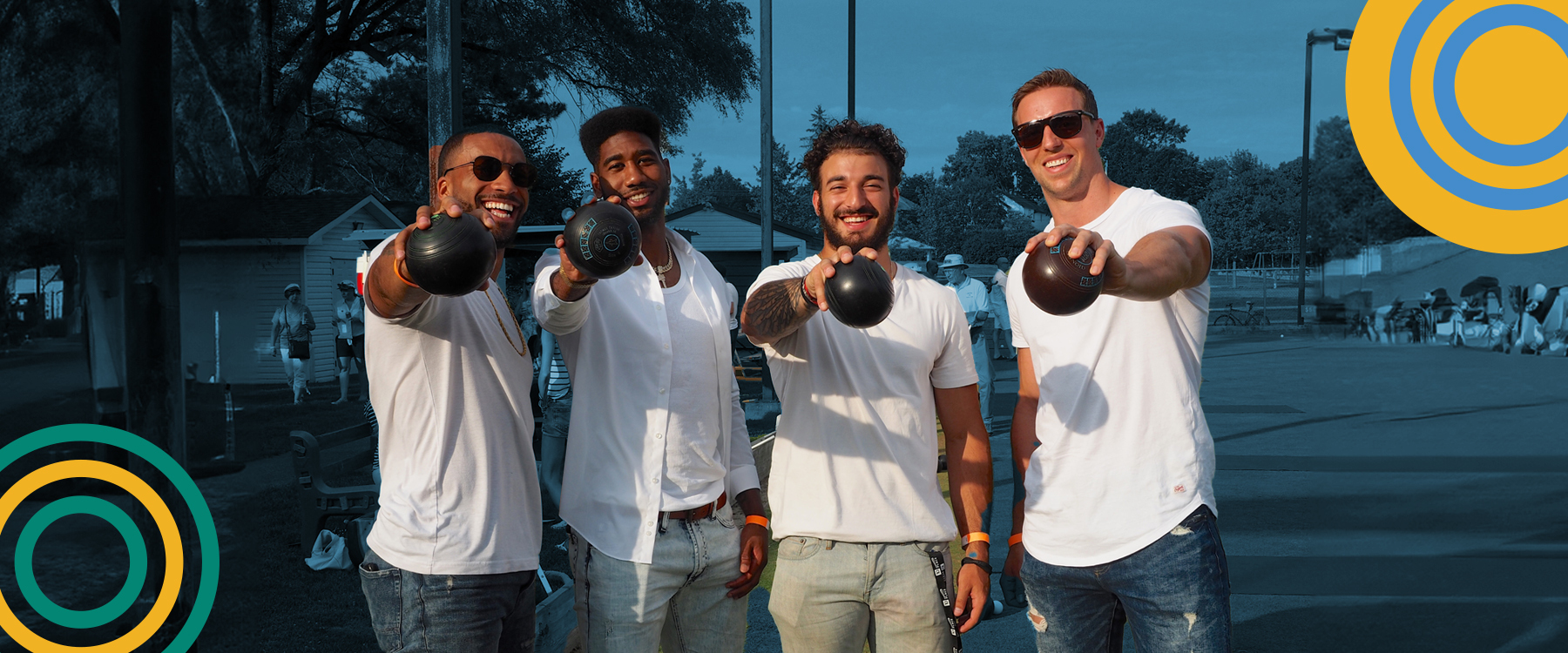 Four male lawn bowlers hold up their bowling balls to the camera.