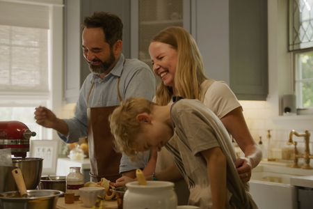 A family of three laughing while baking in their kitchen.